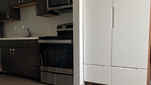 Une cuisine moderne avec des meubles de couleur sombre, des appareils en acier inoxydable et un réfrigérateur blanc.