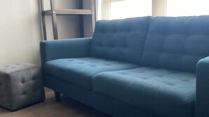 Un canapé bleu, un pouf gris et une étagère en bois dans une pièce dont le sol est également en bois.