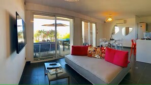 A living room with a sofa, a coffee table, a TV, and a sliding glass door leading to an outdoor area with a table and chairs. - Waterfront apartment, the sea 10 metres away! (La Ciotat)