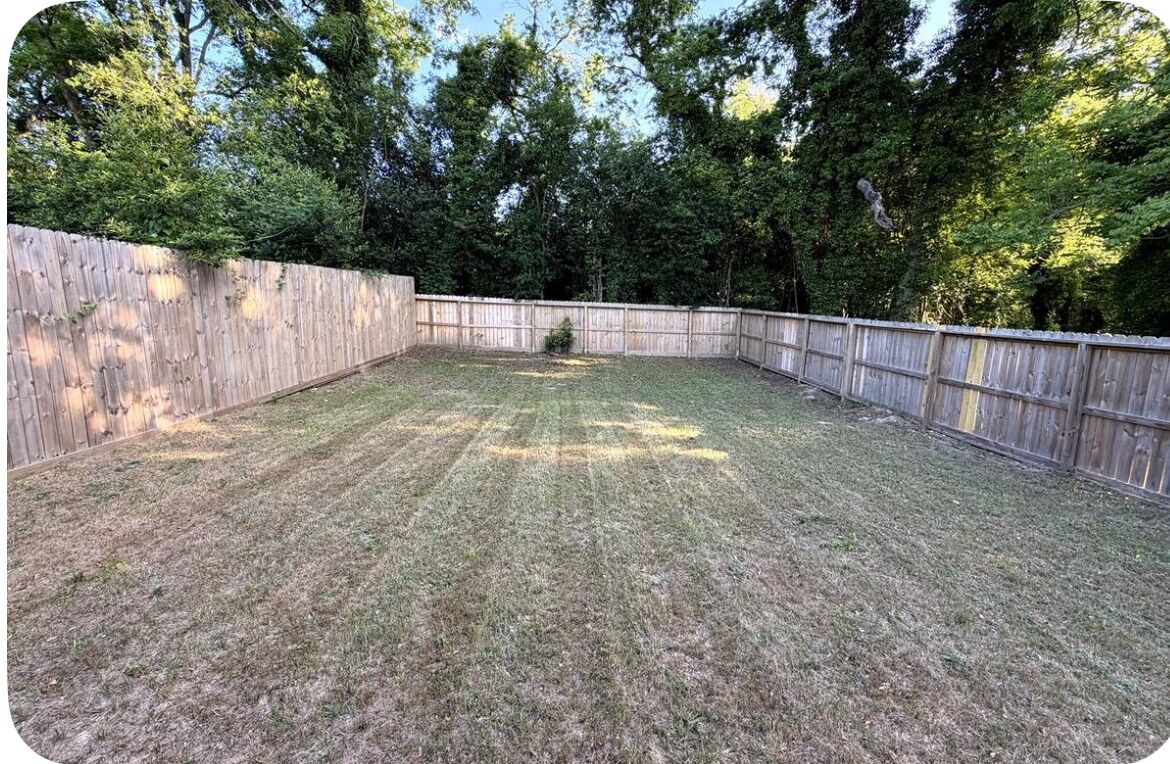 A fenced backyard with a grassy area and trees in the background.