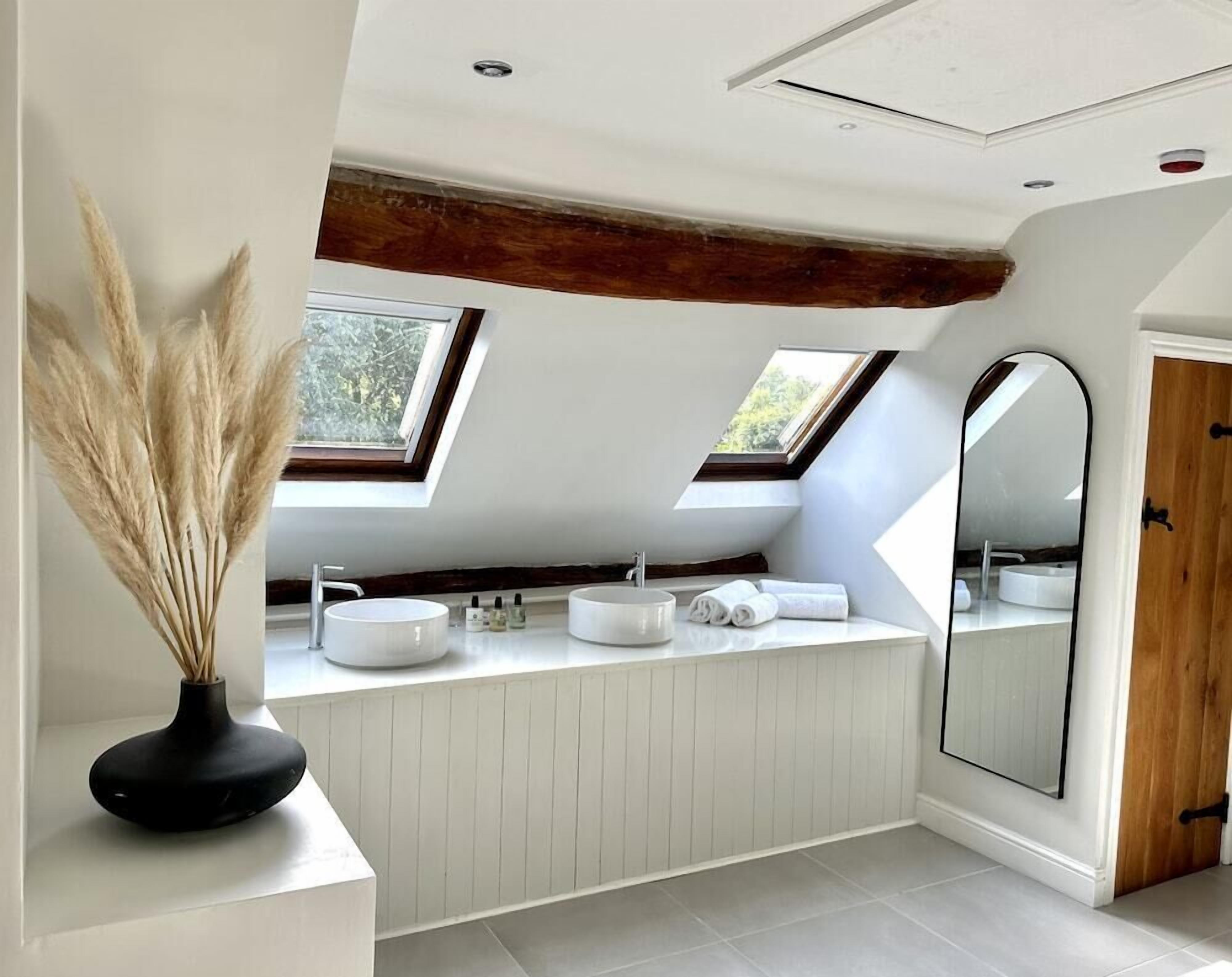 A modern bathroom with skylights, a large mirror, and a black vase with pampas grass.