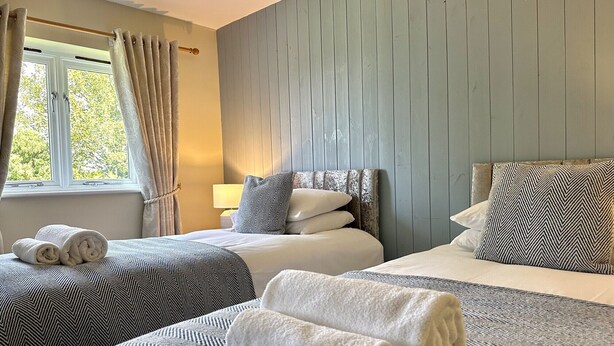 Ett hotellrum med två sängar, ett fönster med gardiner och en sänggavel.