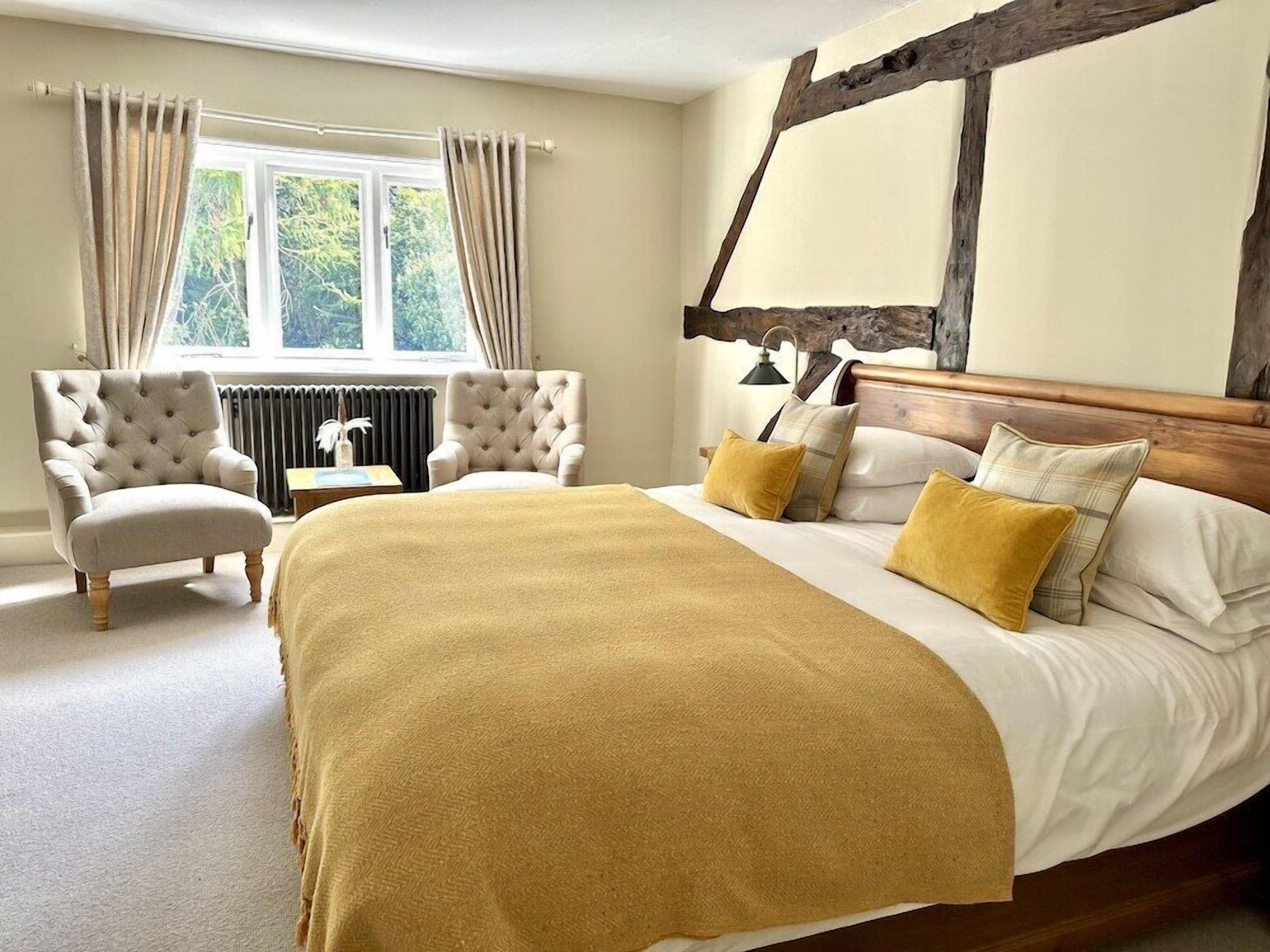 A bedroom with a large bed, two armchairs, a radiator, and a window with curtains.