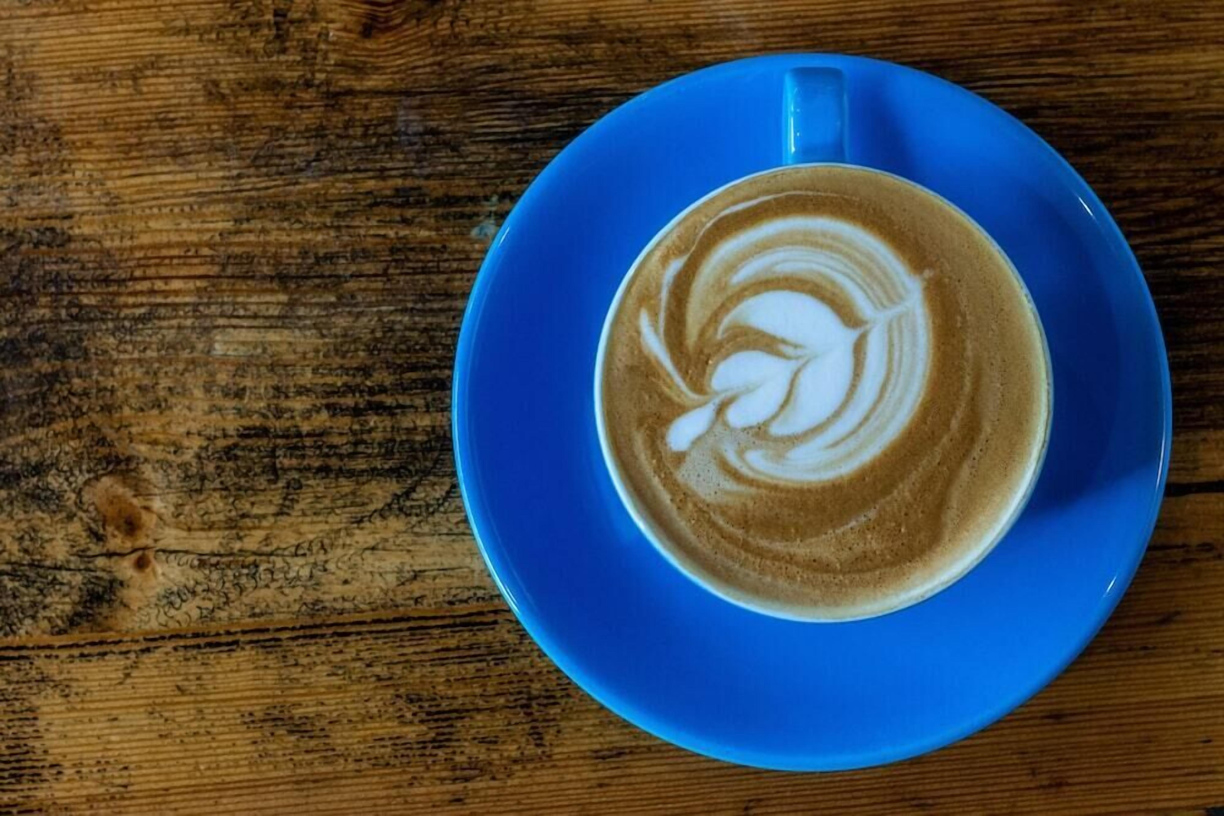 Una taza de café sobre un platito azul sobre una mesa de madera.