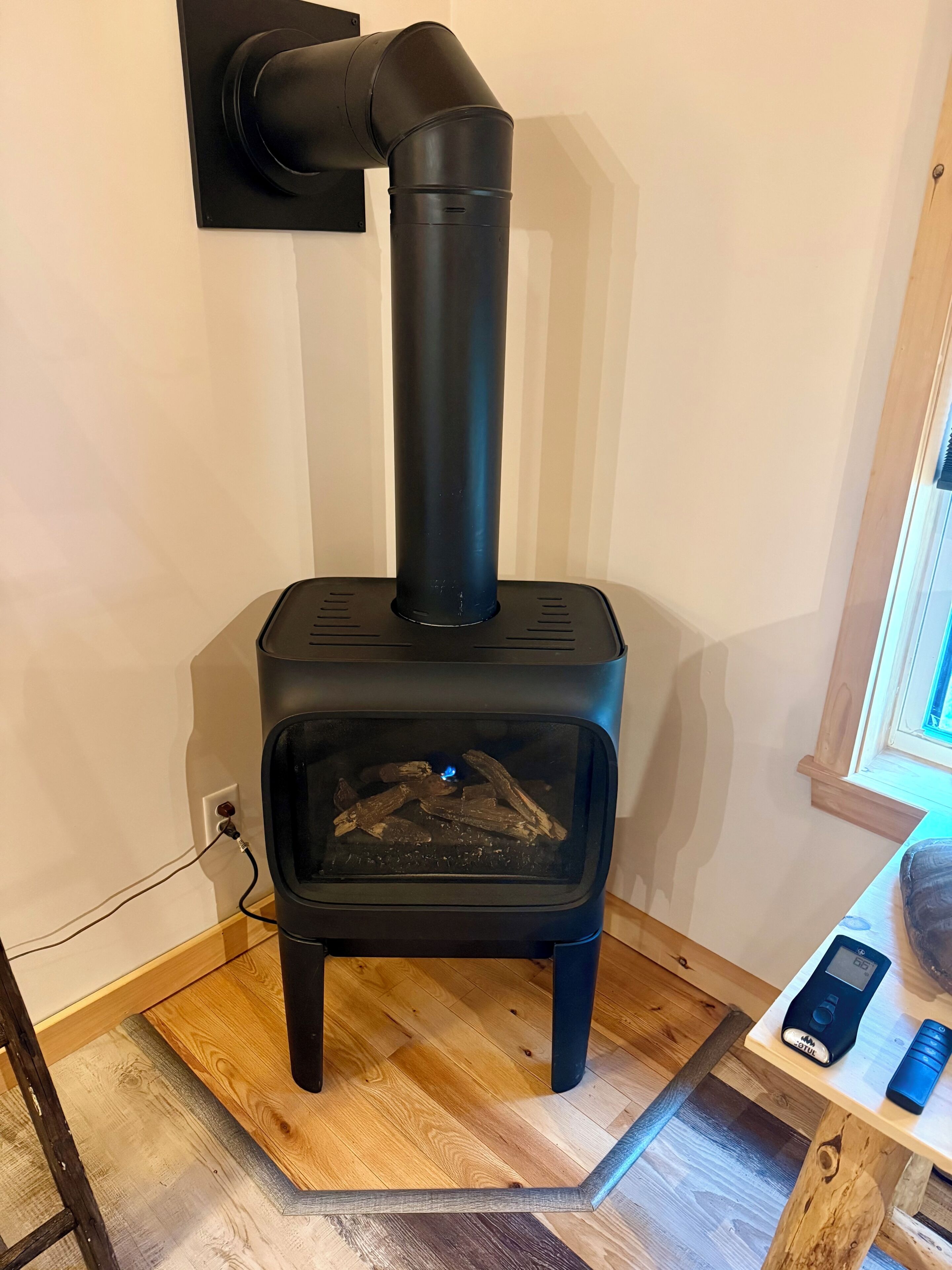 Un poêle à bois avec une cheminée, une prise de courant et un panneau de commande, le tout installé sur un plancher en bois.