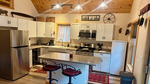 Una cucina moderna con elettrodomestici in acciaio inossidabile, mobili bianchi, un'isola centrale con sgabelli e un soffitto in legno.