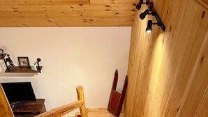 Una scala in legno con gradini rivestiti di tappeto rosso, una ringhiera in legno e un lampadario fissato al muro.