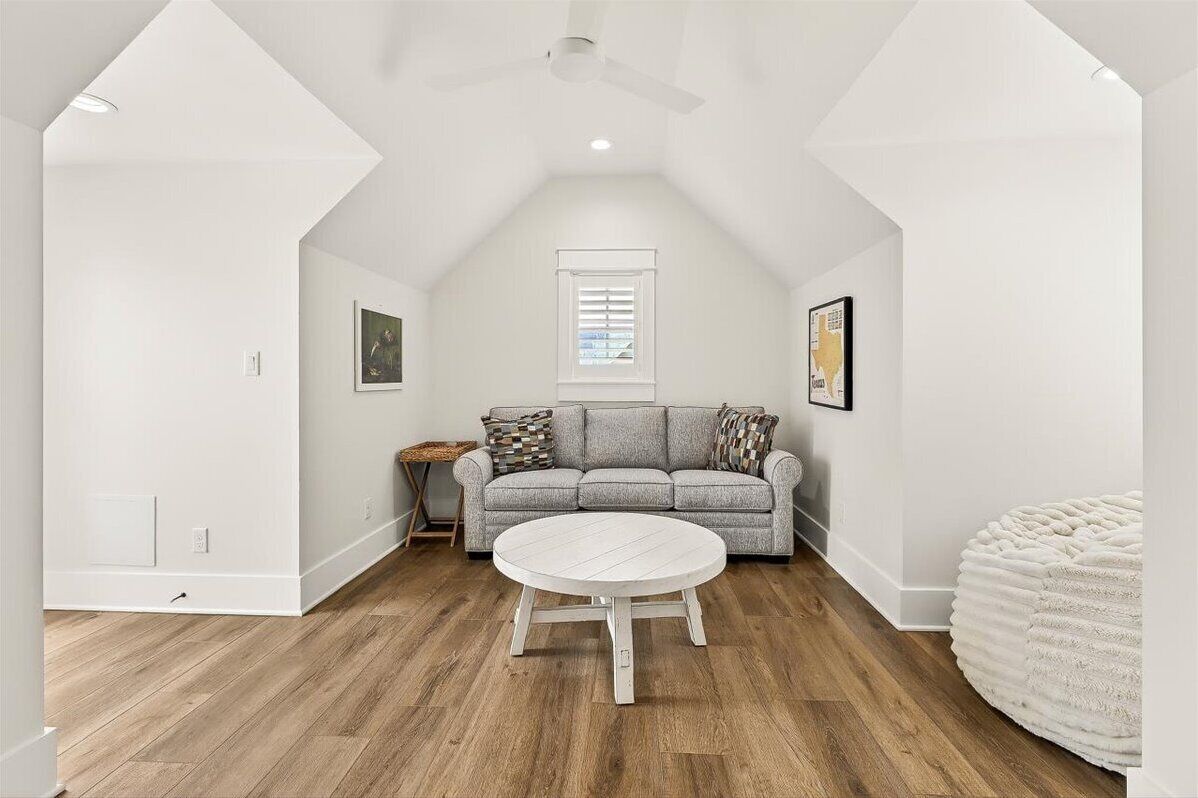 A spacious attic room with a high ceiling, a gray sofa, a round white table, and a round white ottoman.
