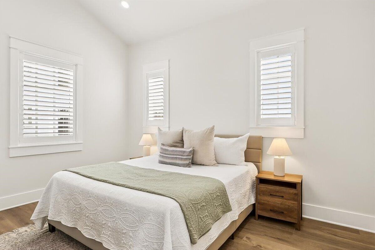 Quarto com uma cama, duas luminárias de cabeceira, mesa de cabeceira e janela com persianas.