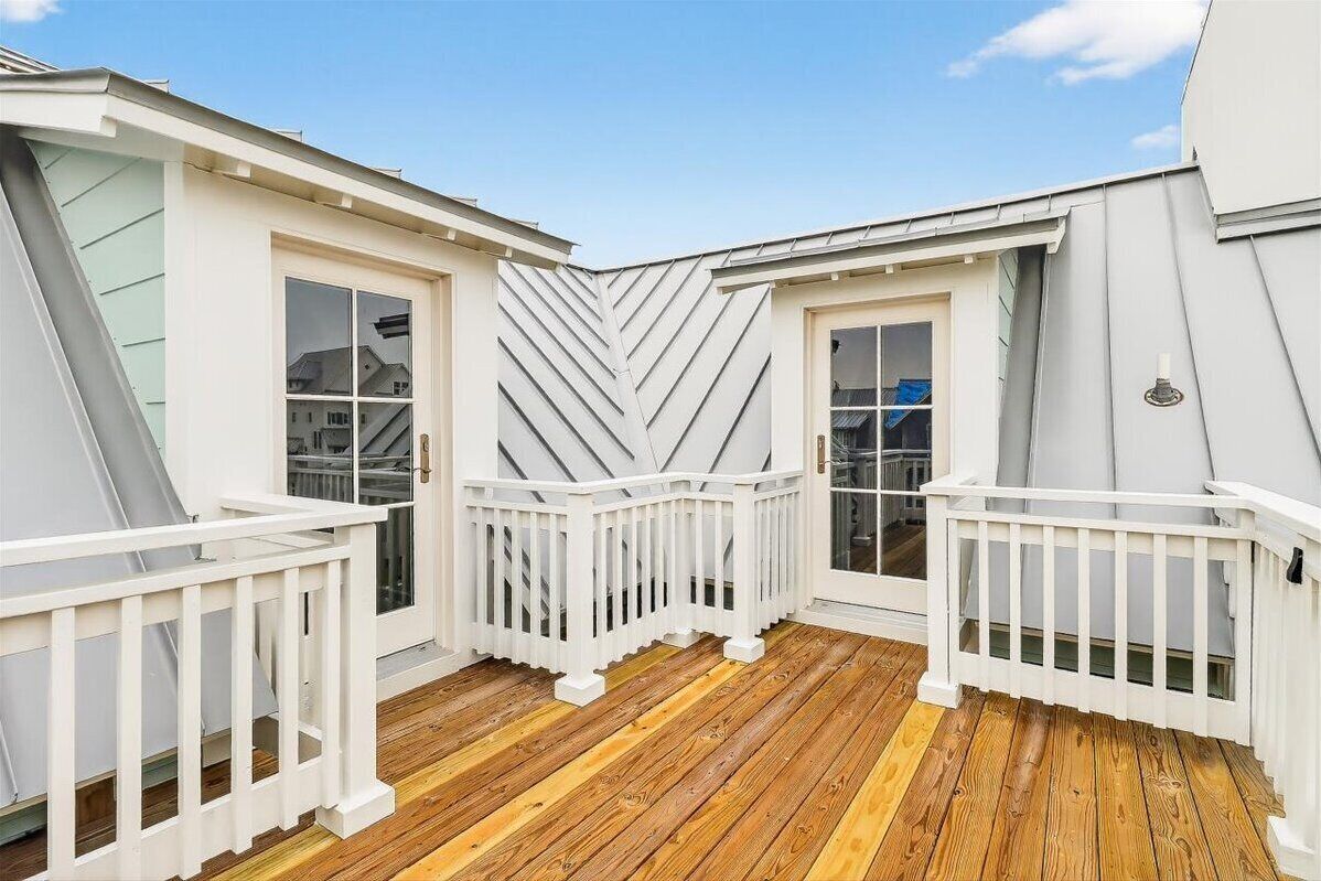 A covered deck with white railings and a wooden floor, surrounded by white walls and large windows.