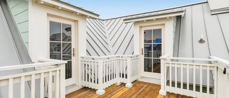 A covered deck with white railings and a wooden floor, surrounded by white walls and large windows.
