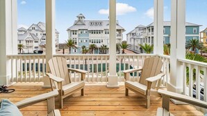 A wooden deck with two Adirondack chairs, a white railing, and a view of coastal houses. - Tortuga House 105 SOU (Port Aransas)