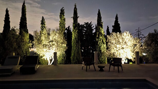 Una piscina con sillones de descanso y un jardín iluminado por la noche.