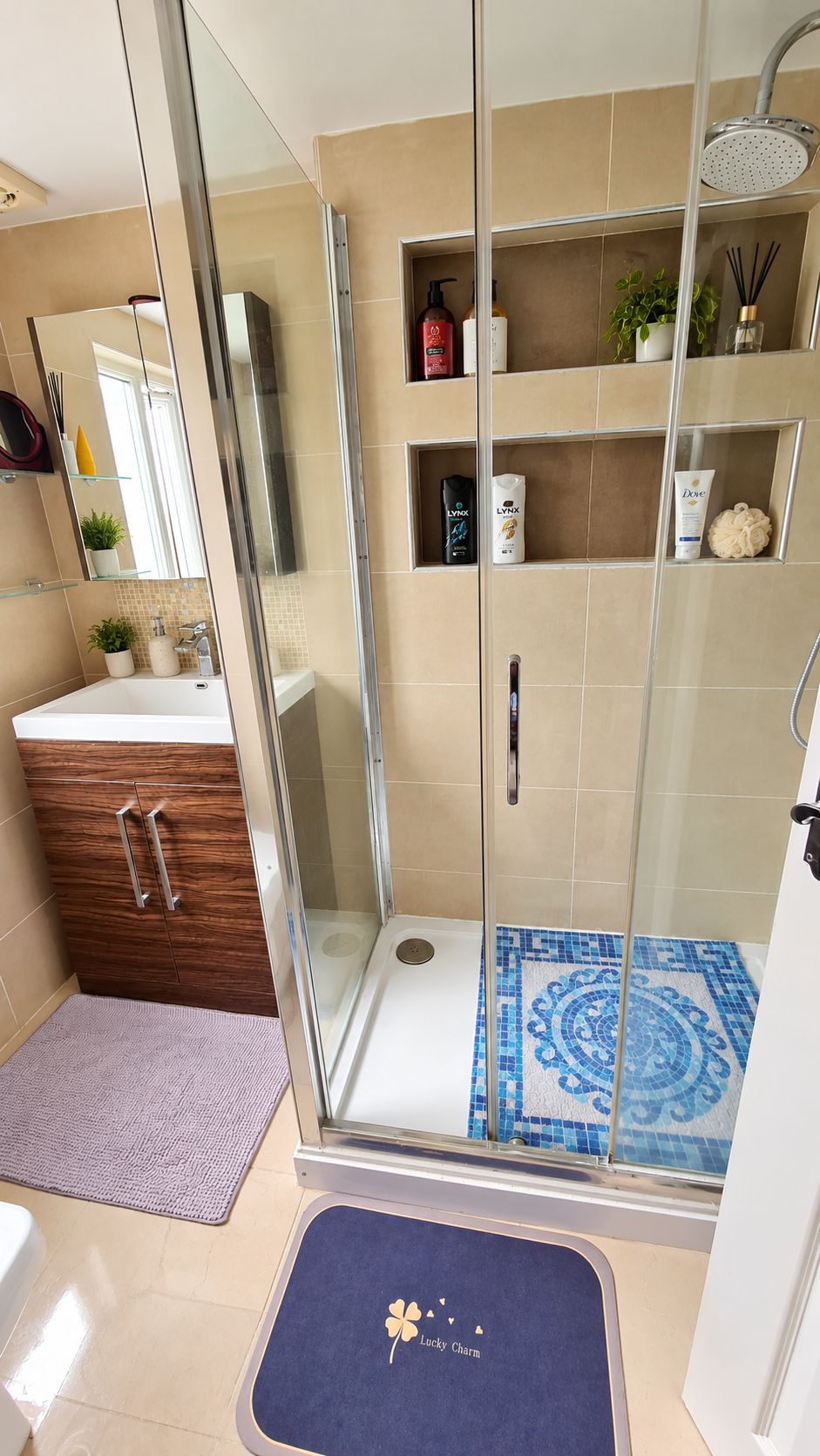 A modern bathroom with a glass shower enclosure, a white sink, and a blue patterned mat.