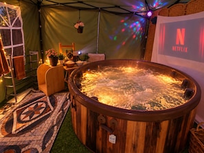 Een hottub met een houten buitenkant, omgeven door een tentachtige constructie met een Netflix-banner.