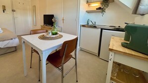 Quarto compacto com mesa de jantar, uma cadeira, pequena cozinha e cama.