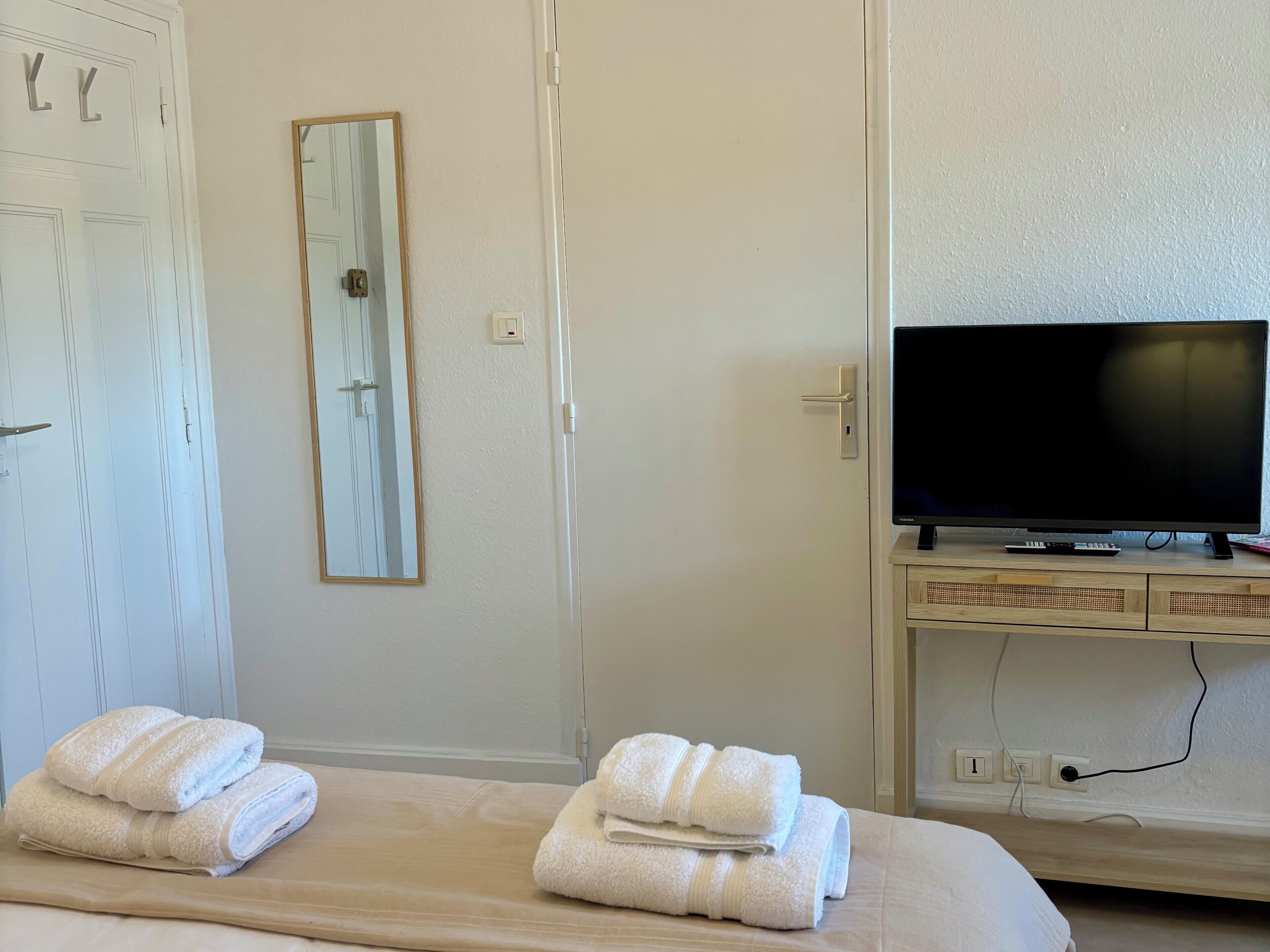 Ein Hotelzimmer mit Bett, Fernseher auf einem Tisch, Spiegel und Handtüchern auf dem Bett.
