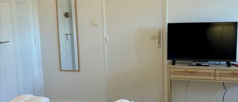 Ein Hotelzimmer mit Bett, Fernseher auf einem Tisch, Spiegel und Handtüchern auf dem Bett.