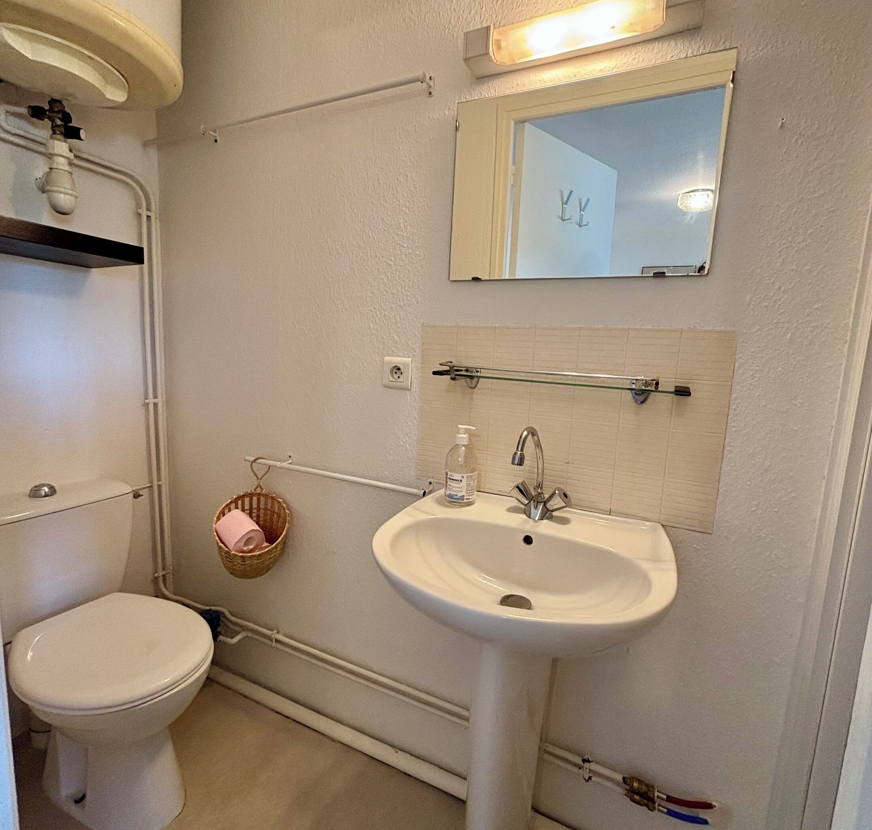 Ein Badezimmer mit Toilette, Waschbecken, Spiegel und einem Korb mit Toilettenpapier.