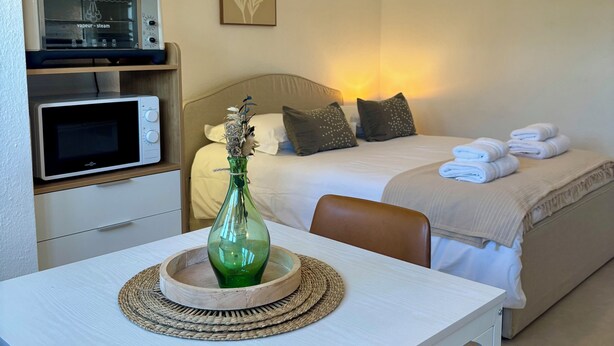 Quarto de hotel com uma cama, micro-ondas, um vaso de flores e uma mesa de cabeceira.