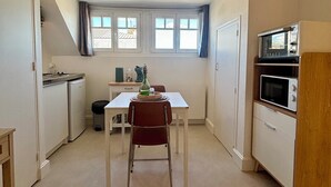 Uma cozinha compacta com mesa, cadeiras, micro-ondas e um refrigerador pequeno.