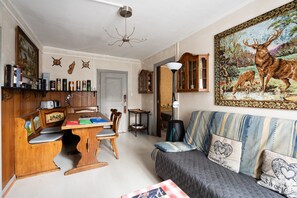A cozy living room with a dining area, a sofa with patterned cushions, and a large painting of a deer.