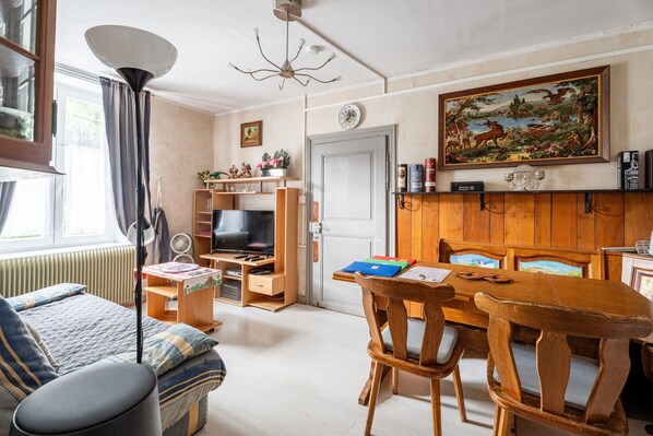 A cozy living room with a sofa, a wooden dining table, a television, and a painting on the wall.