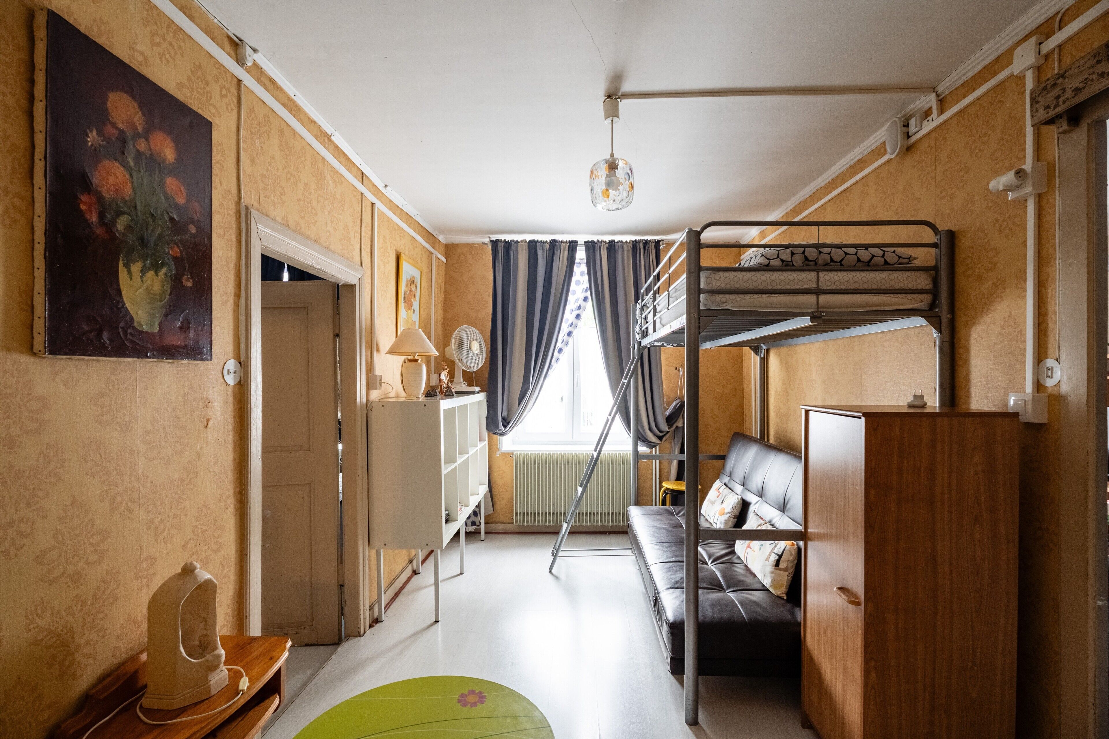 Habitación pequeña con literas, sofá, escritorio y radiador.