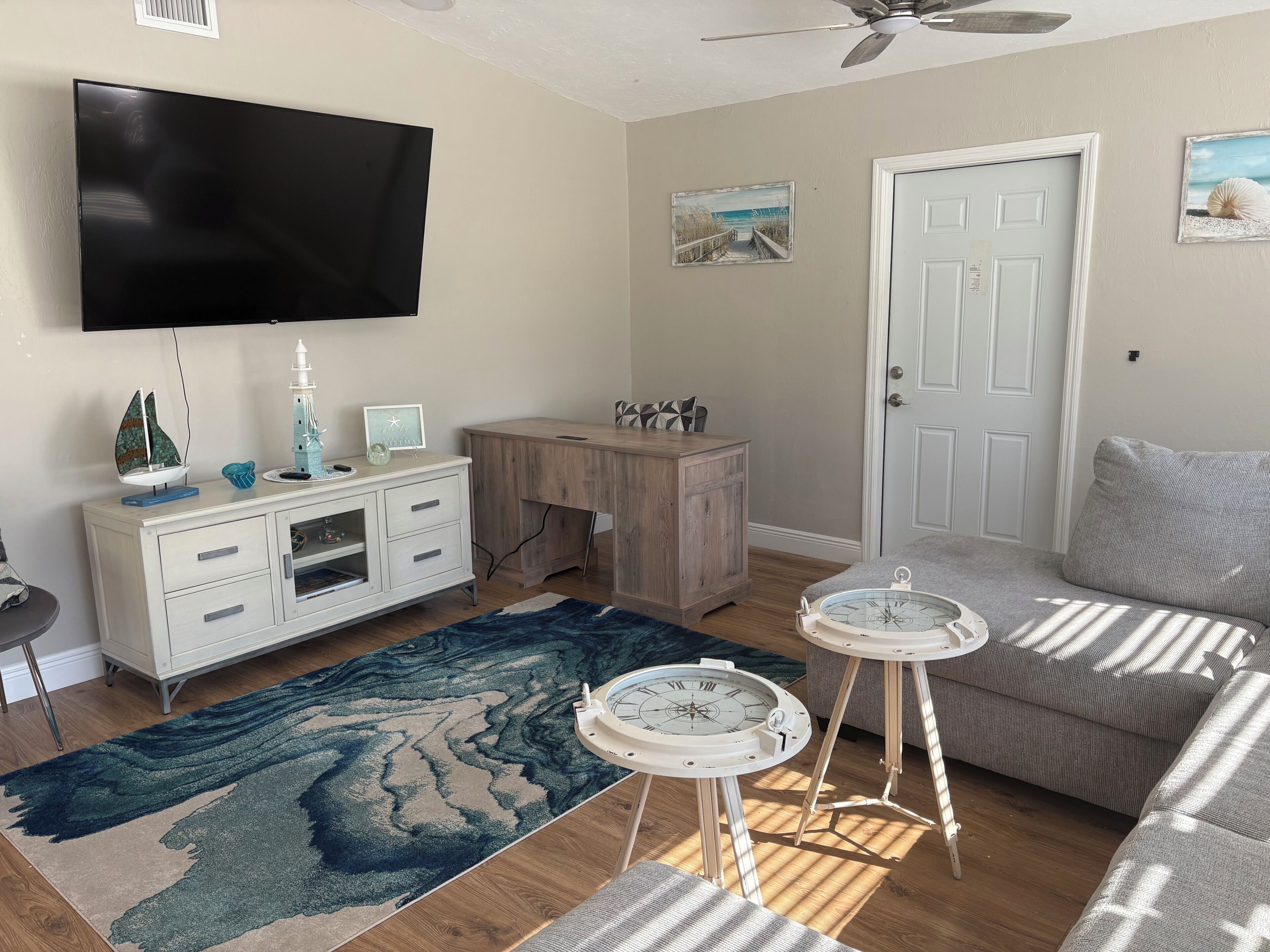 A living room with a TV, a wooden desk, a couch, a rug, and a wall-mounted clock.