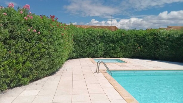 Una piscina con bordo piastrellato, circondata da siepi verdi e un cielo sereno.