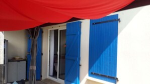 Una stanza con un tendone rosso, una finestra con persiane blu, una porta e un tavolino con una ciotola.