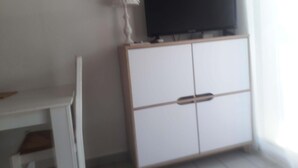 Una stanza con un armadio bianco, una televisione sopra e una scrivania bianca.