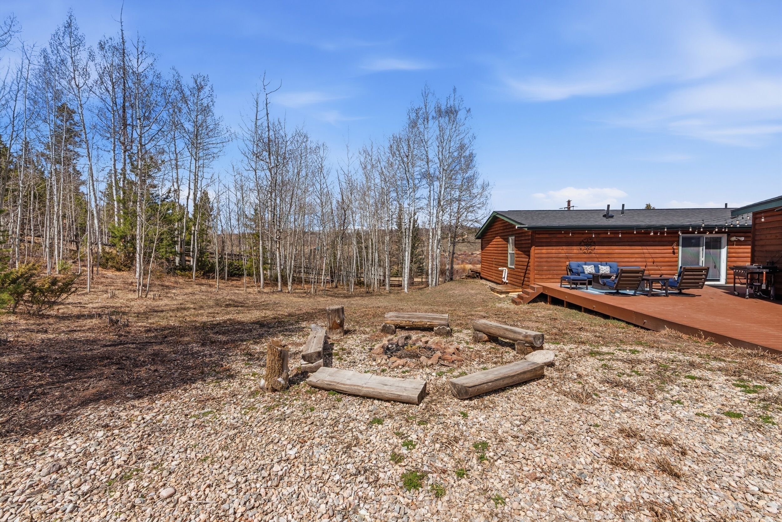 Une cabane dotée d’une terrasse, d’un foyer extérieur et entourée d’une forêt.