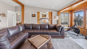 A modern living room with a sectional sofa, a wooden tray, and a stationary bike. - Aspen Grove Cabin - Sauna, 3 Decks, Mountain Views, ATV Access (Grand Lake)