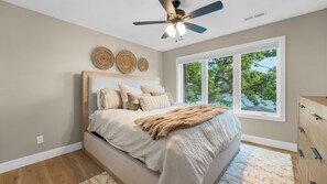 Ein Schlafzimmer mit einem Bett, einem Deckenventilator, einem großen Fenster und einer Holzkommode.