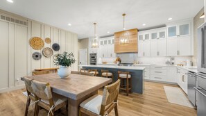 Une cuisine moderne avec des meubles blancs, un îlot central en bois et un coin repas doté de chaises en osier.
