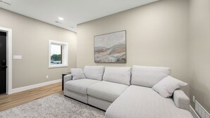 A modern living room with a sectional sofa, a window, a painting, and a patterned rug. - 40’ Boat Slip-New Luxury Lakefront-3 King Beds-Sleeps 12-21MM (Osage Beach)