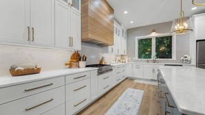 A modern kitchen with white cabinetry, a central island, and a large window providing a view of trees. - 40’ Boat Slip-New Luxury Lakefront-3 King Beds-Sleeps 12-21MM (Osage Beach)