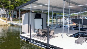 Eine überdachte Anlegestelle mit Tisch und Stühlen, ein kleines Gebäude mit einer Tür und ein Boot im Hintergrund.