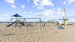 A beach with a swing set, a lighthouse, and a blue umbrella.