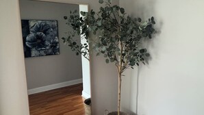A hallway with wooden flooring, a potted plant, and a painting on the wall.