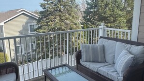 A balcony with a wicker sofa, a glass coffee table, and a patterned rug.