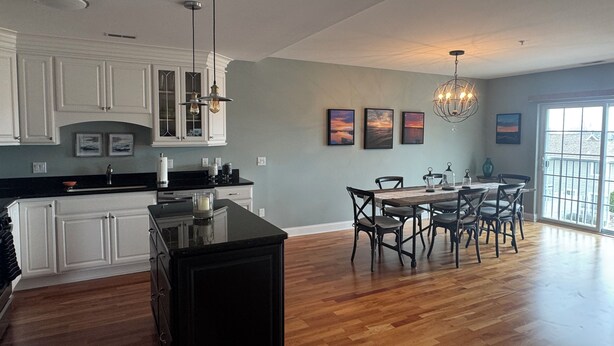 A spacious kitchen with white cabinetry, a black island, and a dining area with a table and chairs.
