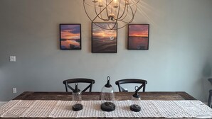 A dining table with a woven placemat, two chairs, and a chandelier with multiple bulbs.