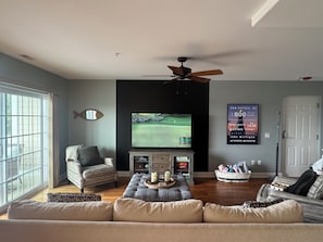 A living room with a television, a ceiling fan, and a poster on the wall.