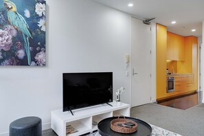 Ein modernes Wohnzimmer mit einem Flachbildfernseher auf einem weißen Schrank, einem runden Couchtisch mit einem Korb und einem Papageienbild an der Wand.
