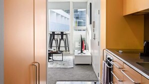 En smal gang der fører til en balkon med stole, et lille bord og et fjernsyn.