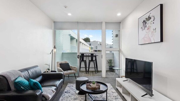 En moderne stue med sofa, fjernsyn, sofabord og en balkon med stole.