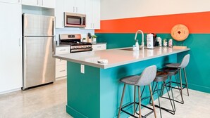 Een moderne keuken met een centraal eiland, roestvrijstalen apparatuur en een kleurrijke accentmuur.