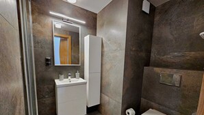 Une salle de bain moderne avec une douche à l’italienne en verre, un lavabo blanc avec un miroir au-dessus et des toilettes.